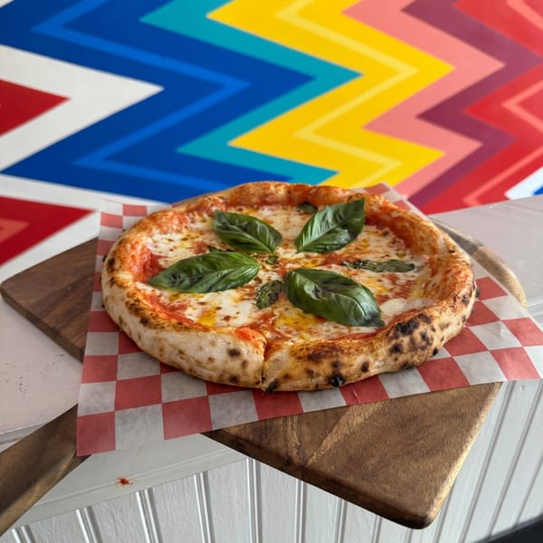 A Neapolitan pizza with fresh basil leaves and melted mozzarella on a wooden board.