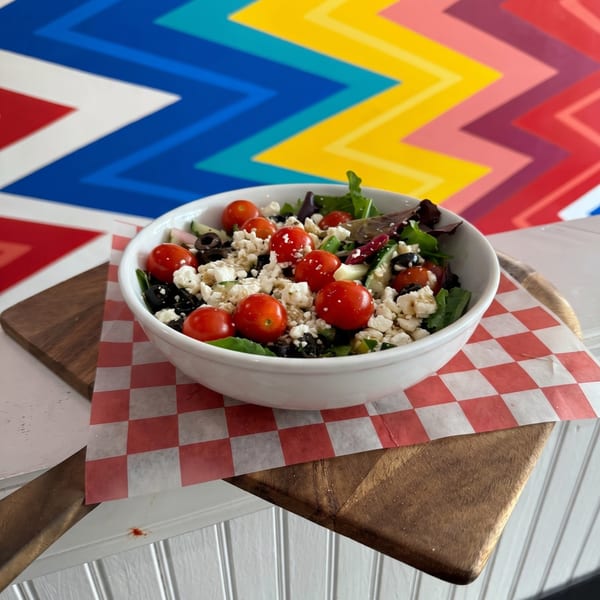 A fresh salad with cherry tomatoes, feta cheese, and olives in a white bowl on a wooden board.